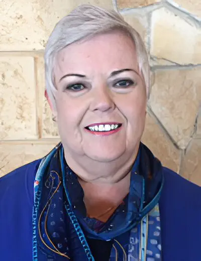 A smiling woman with short gray hair wearing a blue top and a patterned scarf.