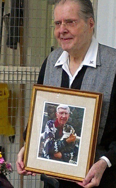 A person holding a framed photograph of someone holding a bird.