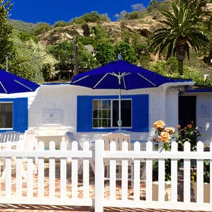 A white fence with blue shutters and umbrellas.